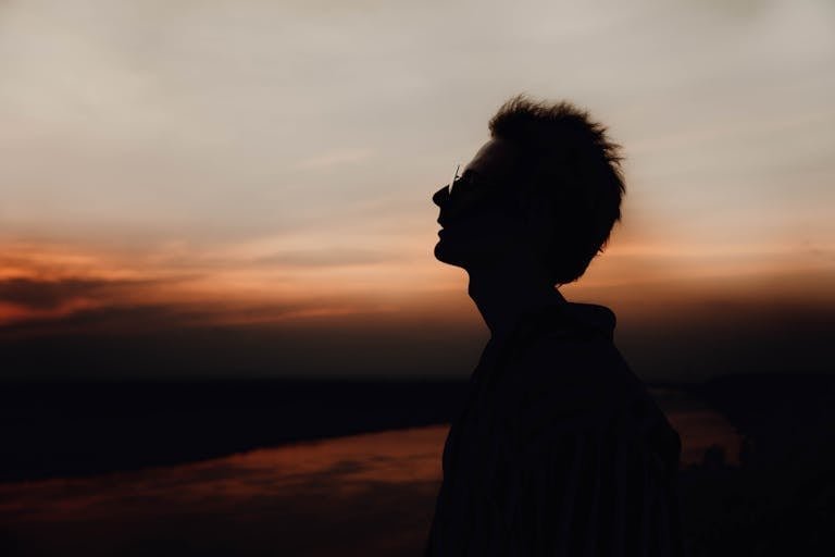 Side view of lonely male silhouette in eyeglasses breathing and admiring cloudy sky at night