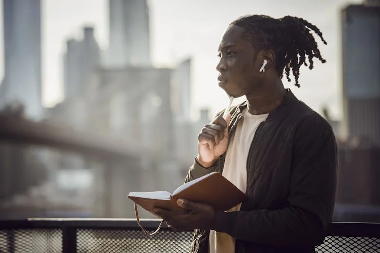 Thoughtful black man in wireless earphones with notepad on balcony - intentional living