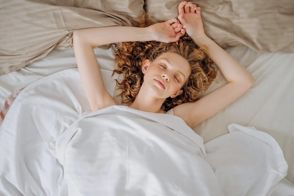 Woman With Curly Hair Lying Down on Bed With White Blanket